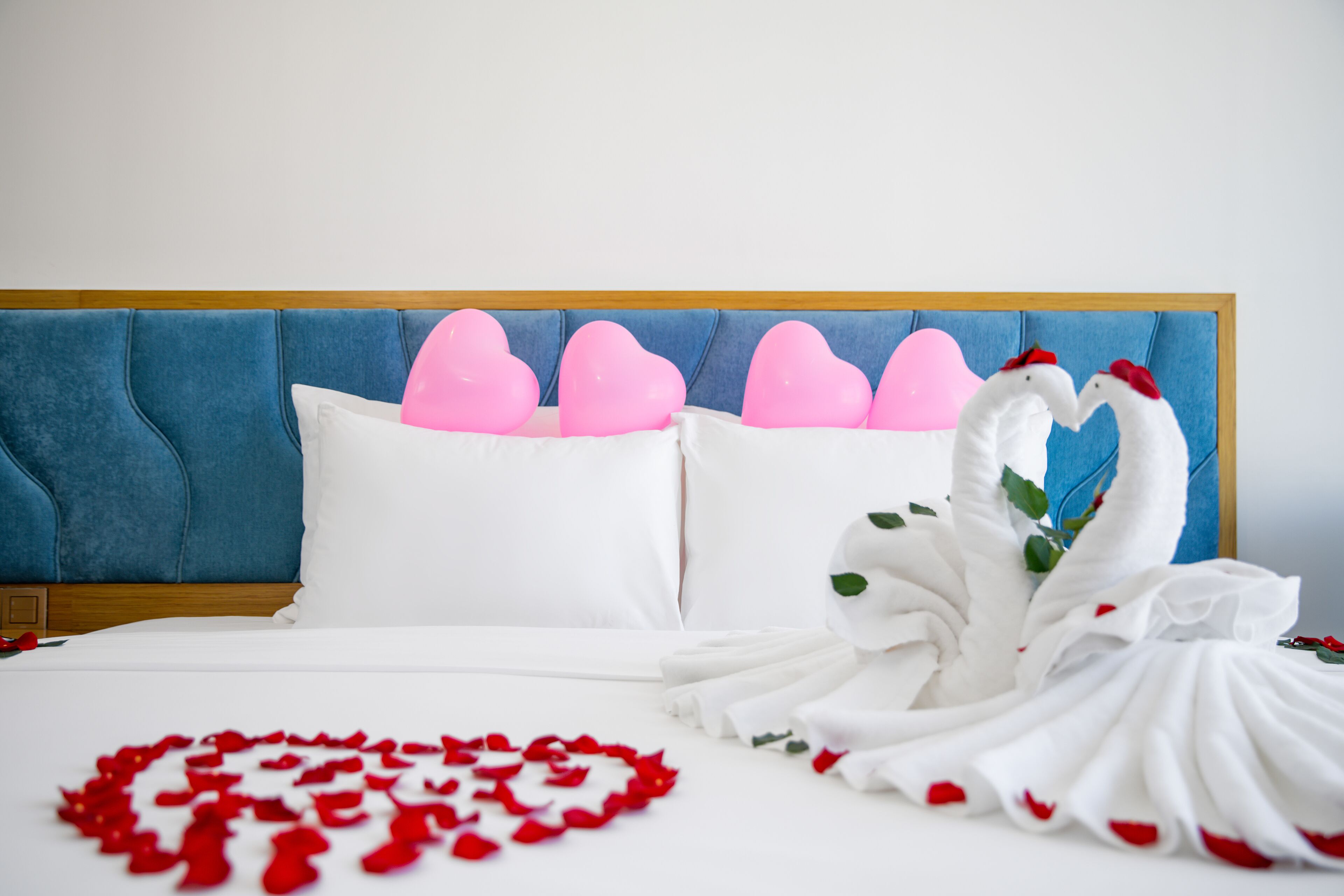 A hotel room with a blue headboard, white bedding, and decorative swans made of fabric.