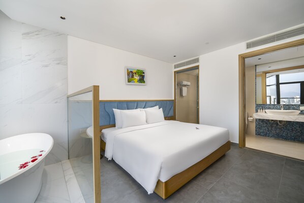 A modern hotel room with a large bed, a separate bathroom, and a view of the city.