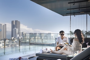 A rooftop pool area with a cityscape view, lounge chairs, and a glass barrier.