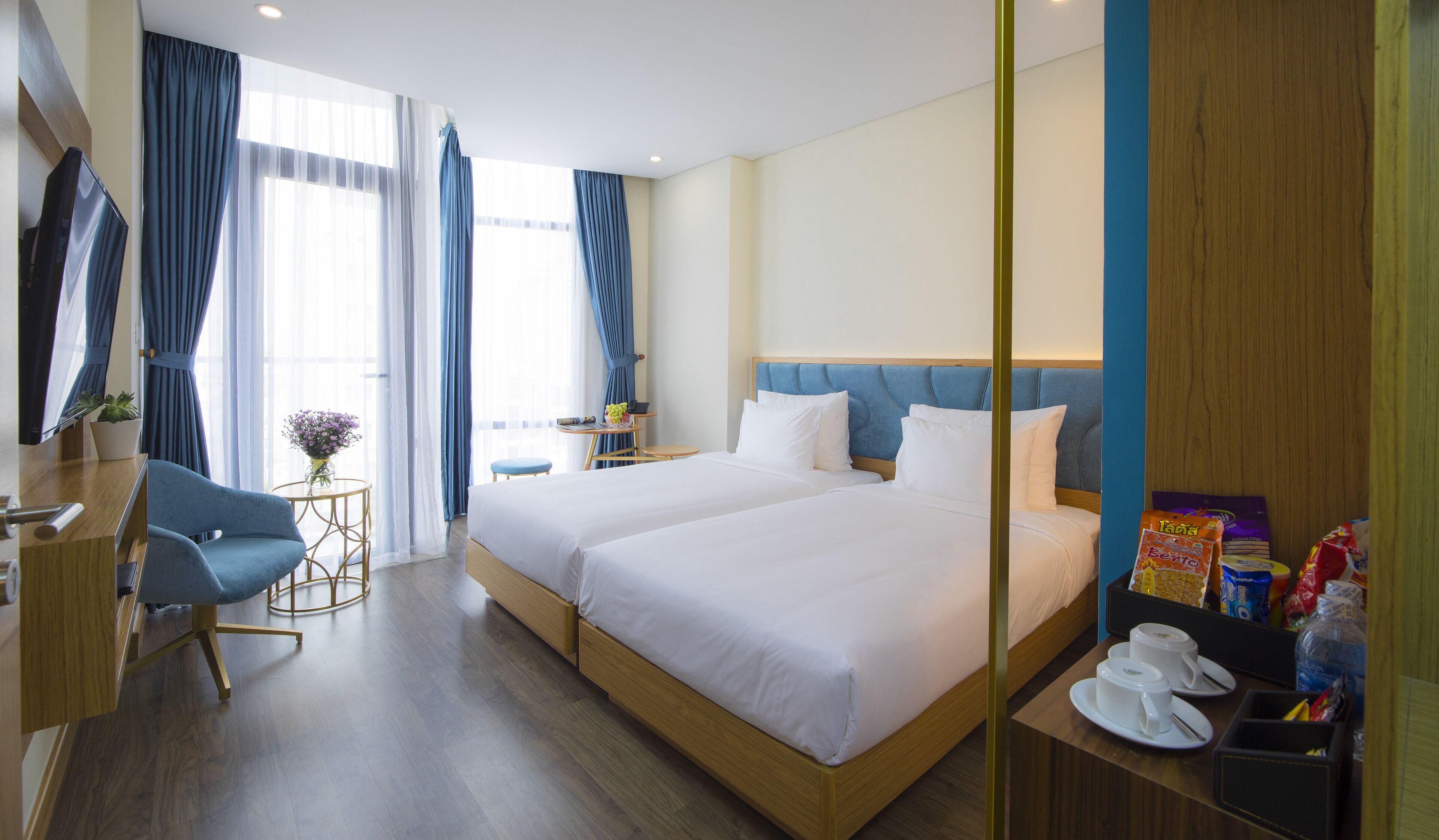 A hotel room with two beds, a desk, a chair, a TV, and a window with curtains.
