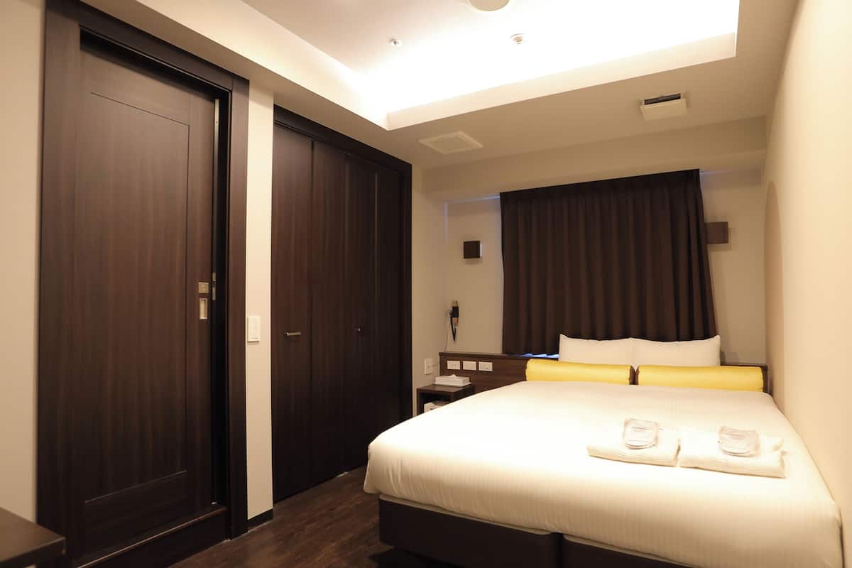 A hotel room with a large bed, a nightstand, a desk, and a wardrobe.
