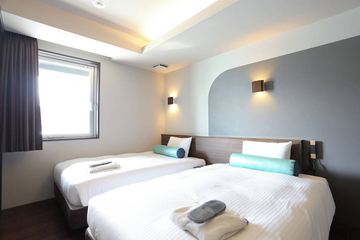 A hotel room with two beds, a large window, and a modern design.