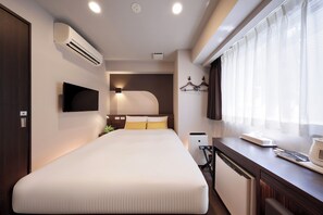 Una moderna camera d'albergo con un letto grande, una TV a schermo piatto, un comodino con una lampada, una piccola angolo cottura e una finestra con tende leggere.
