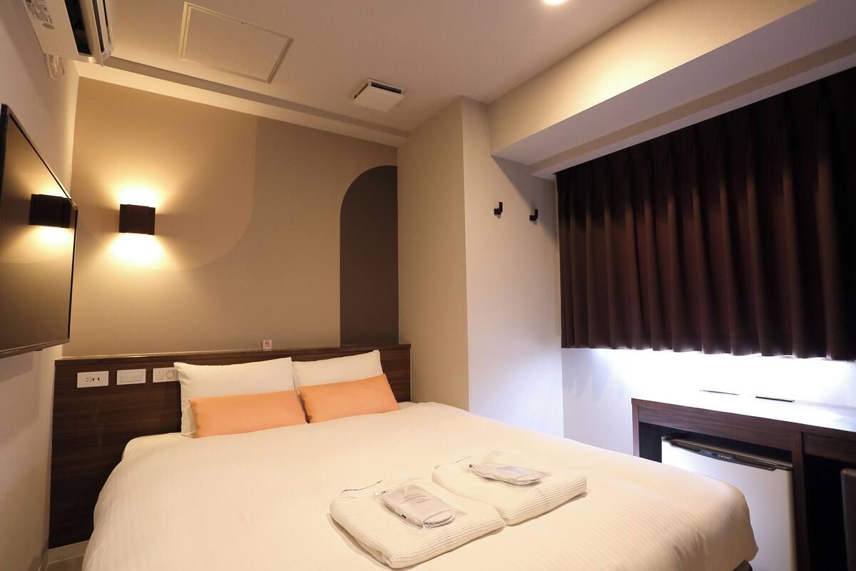 A hotel room with a neatly made bed, a bedside table with a lamp, and a window with curtains.