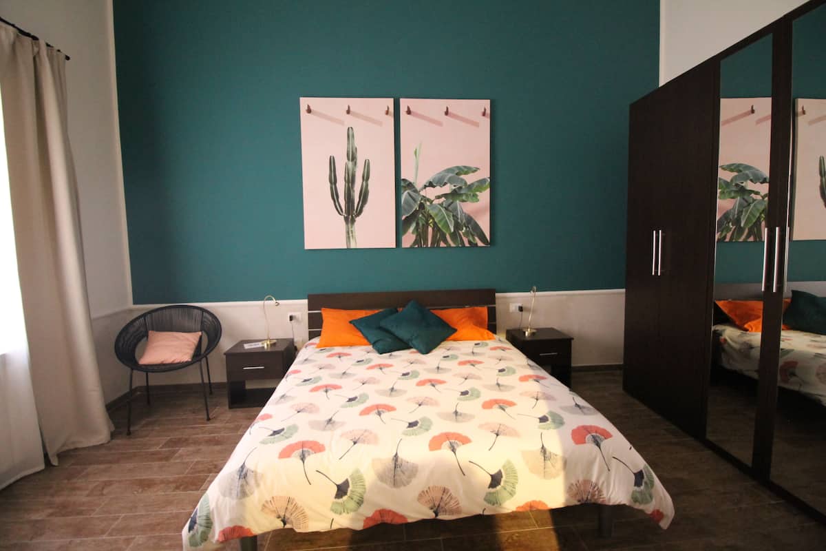 A bedroom with a bed, nightstands, a chair, and a wardrobe.
