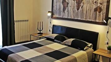 Ein ordentlich bezogenes Bett mit schwarzem Kopfteil, ein Weltkarten-Kunstwerk darüber, ein Nachttisch mit Lampe und ein Heizkörper an der Wand.