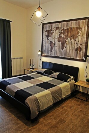 A neatly made bed with a black headboard, a world map artwork above it, a bedside table with a lamp, and a radiator on the wall. - Il Civico 2 (Bari)