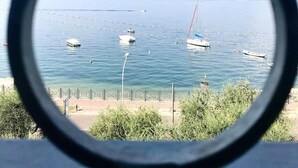 A view through a circular window of a marina with boats, a clear sky, and distant mountains. - Hotel Garden (Torri del Benaco)