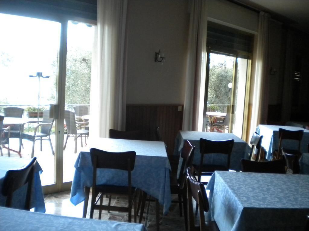 Zona pranzo con tavoli ricoperti da tovaglie blu, sedie e un'ampia finestra con tende.