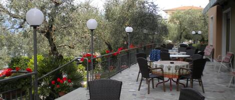 An outdoor patio with round tables and wicker chairs, surrounded by a metal railing and potted plants.