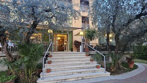 A hotel entrance with a staircase leading to a green door, surrounded by olive trees and potted plants. - Hotel Garden (Torri del Benaco)