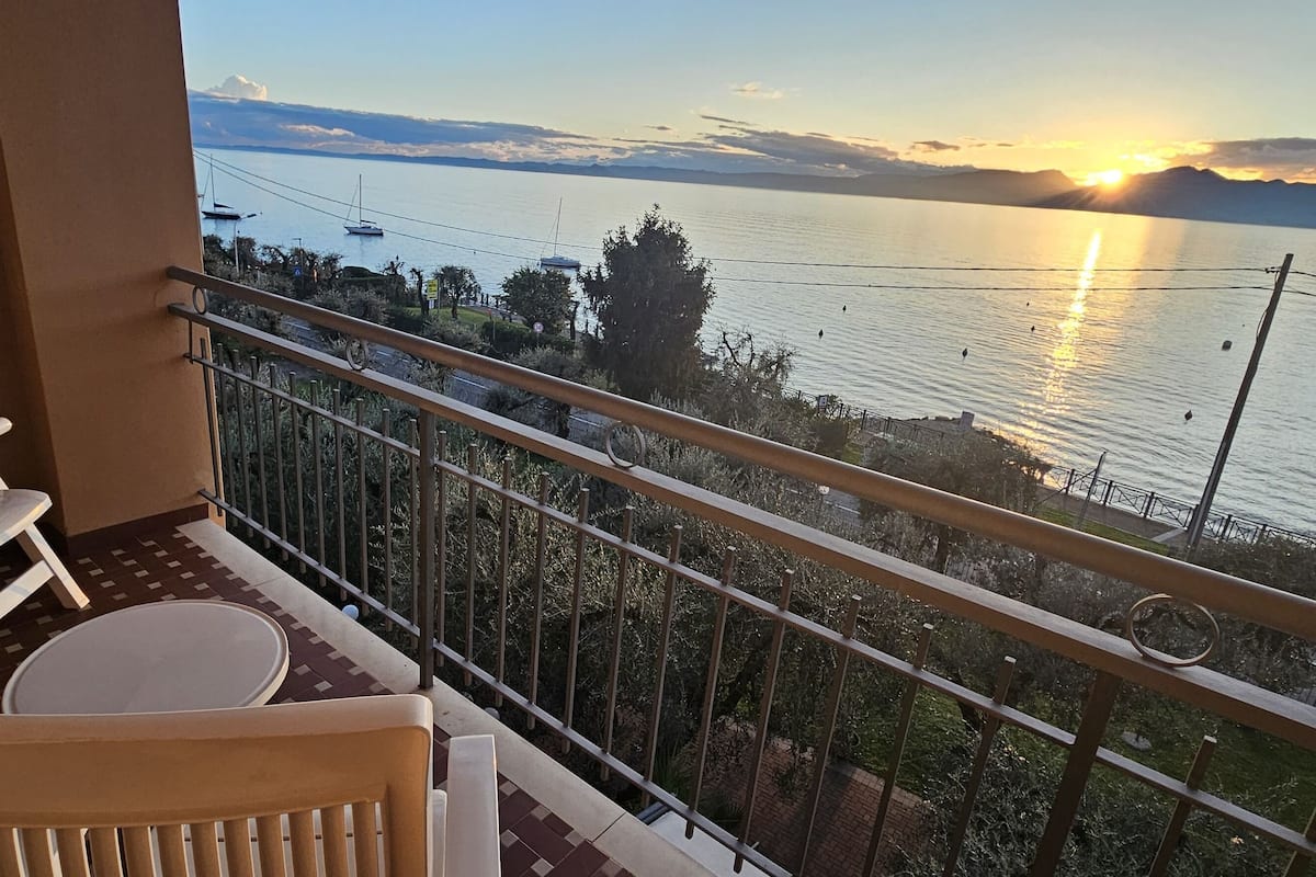 A balcony with a view of the sea, a table, and two chairs.