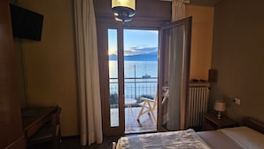 A hotel room with a bed, a desk, a chair, a table, and a view of the sea through an open door. - Hotel Garden (Torri del Benaco)