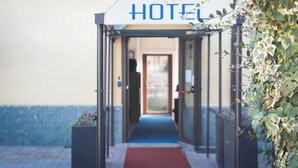 A hotel entrance with a sign reading "HOTEL" above a glass door, a red carpet leading inside, and a wall with climbing plants. -  La Boheme SMART Hotel (Turin)