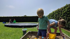 A child playing with sand in a sandbox with toys and a trampoline in the background. - Flanders Fields Cottage Leisele (Alveringem)