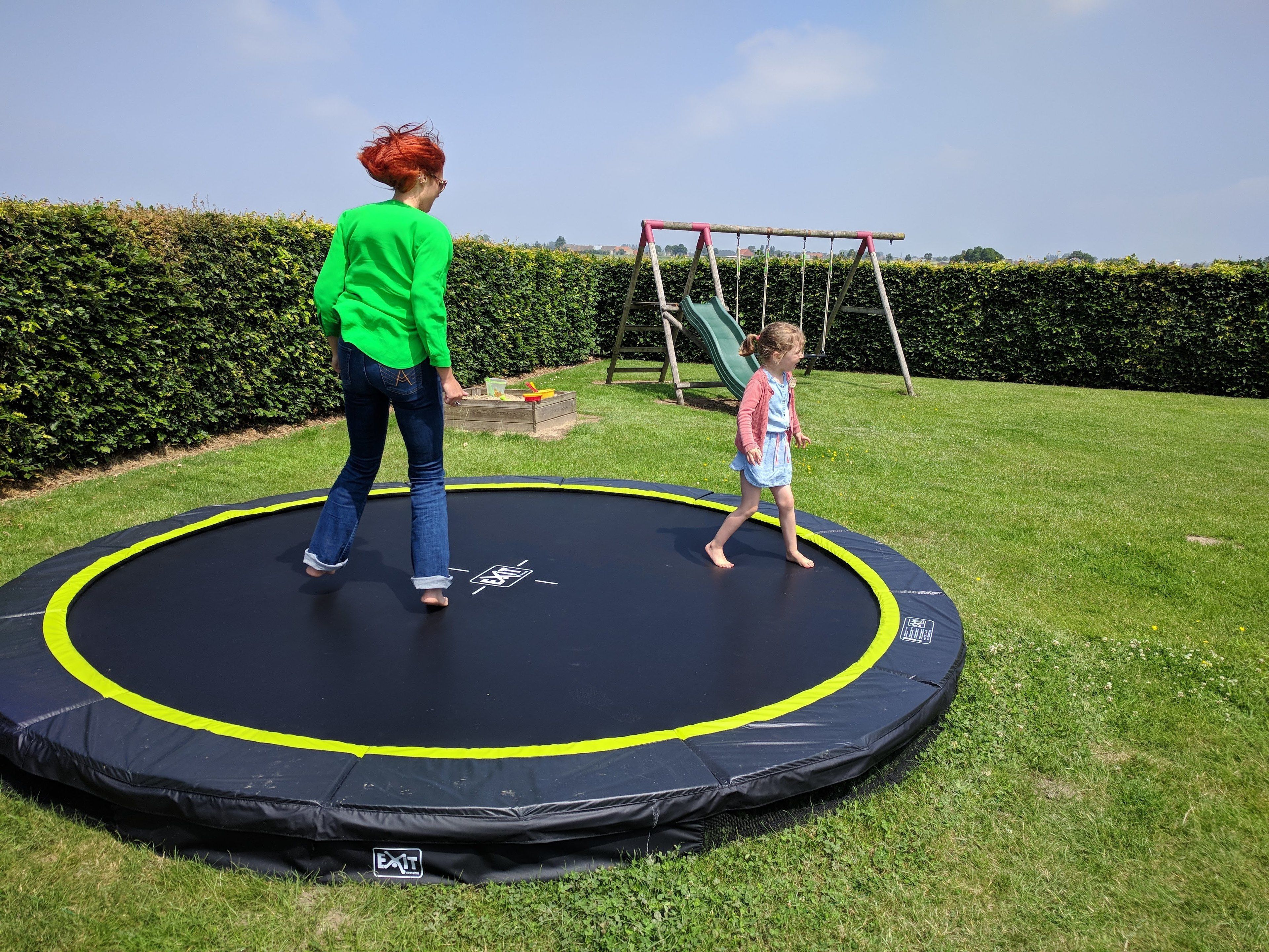 Un trampolín en una zona con césped, con un columpio al fondo.