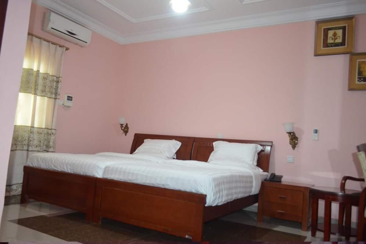 A bedroom with a wooden bed, a nightstand, a chair, and a wall-mounted lamp.