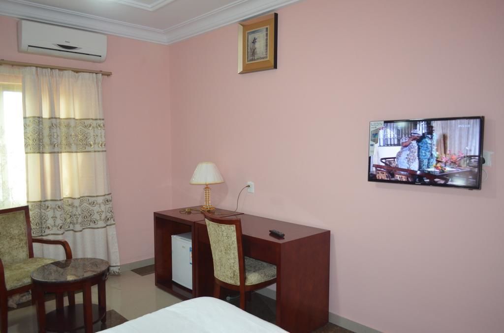 A hotel room with a bed, a desk with a lamp, a chair, a television, and an air conditioning unit.