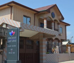 A two-story building with a sign for "Precious Guest Lodge" indicating a luxury room, bed, and breakfast fast service. - Precious Guest lodge (Accra)