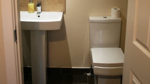 Et lille badeværelse med håndvask, spejl, toilet og et opmuntrende citat på væggen.