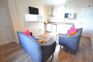 A compact living space with two grey sofas, a small kitchen area, and a white door. - Premier Lodge (Wolverhampton)
