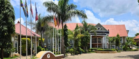 Un hotel con techo rojo, varias banderas, palmeras y un letrero que dice 'Sailand'.