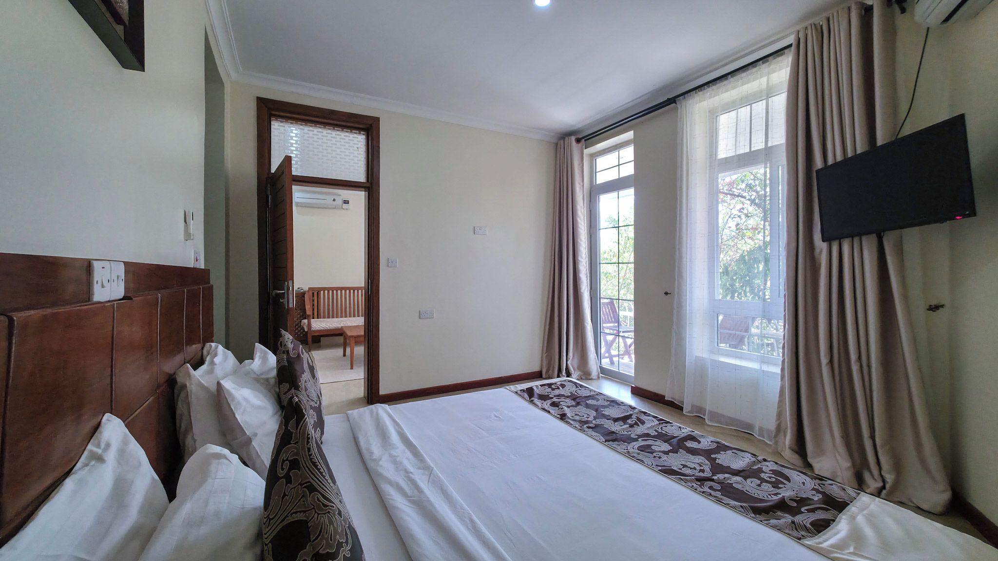 Ein Hotelzimmer mit einem großen Bett, einem an der Wand befestigten Fernseher und Blick ins Freie durch die Fenster.