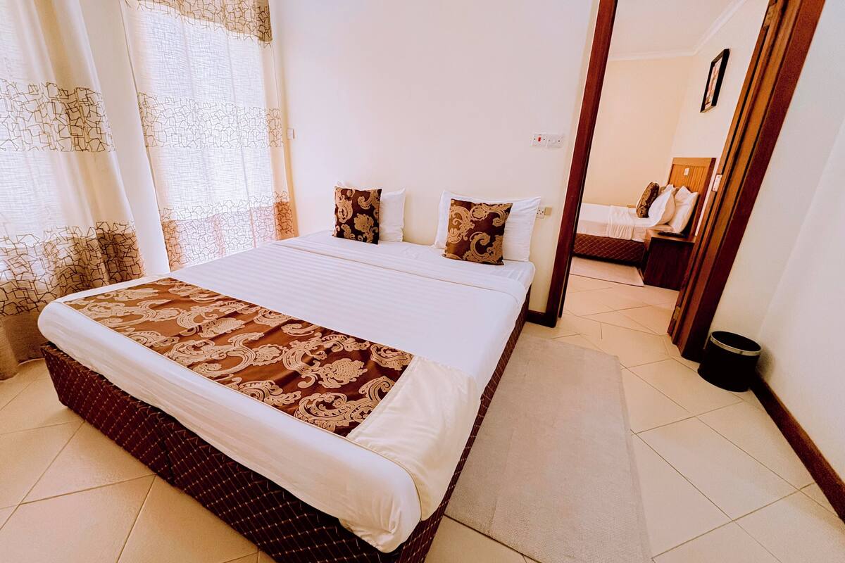 Habitación de hotel con una cama grande, piso de madera y vista hacia la habitación contigua.