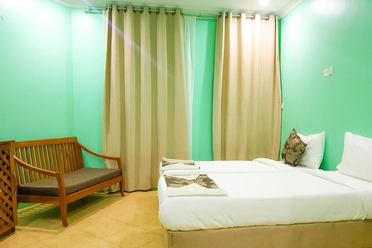 Una habitación con cama, una silla de madera y una ventana con cortinas.