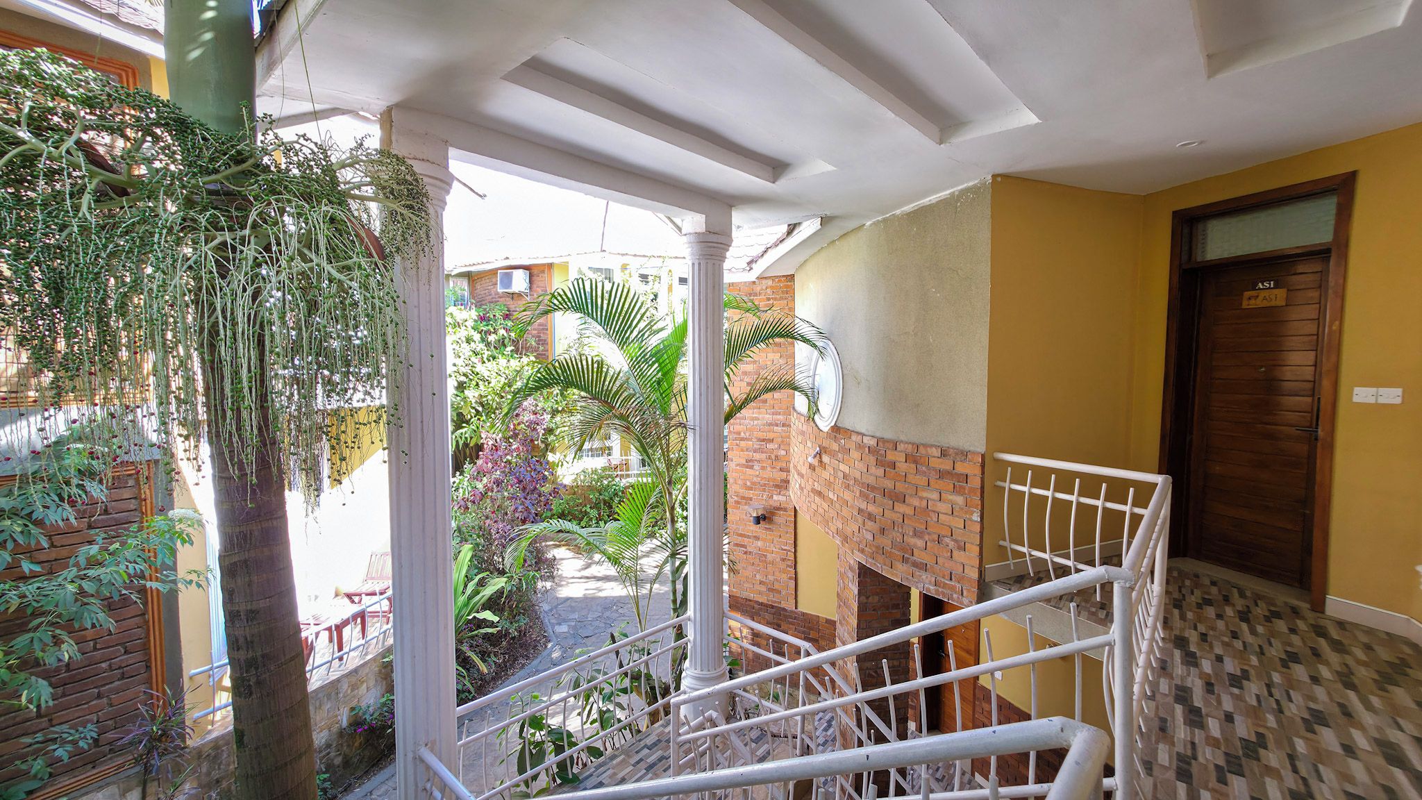 A balcony with a view of a garden and a brick wall.