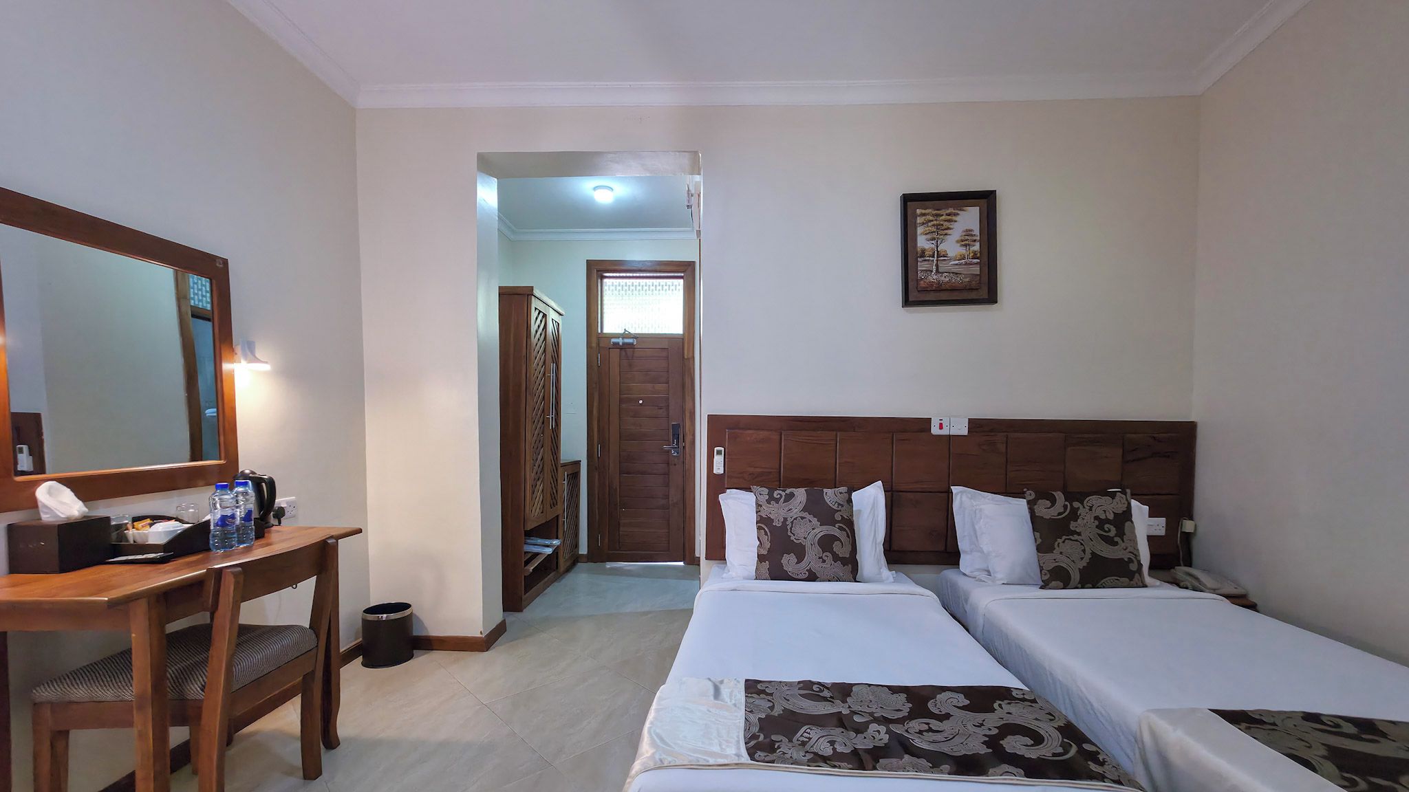 Een hotelkamer met een houten bureau, een bed met gestreepte kussens, een ingelijste foto aan de muur en een deur die naar een andere kamer leidt.