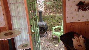 A cozy room with a green door leading to a garden, a small table with a flower-patterned tablecloth, a wicker chair, and a rustic stove. - Frog Hollow Bed and Breakfast (Lexington)