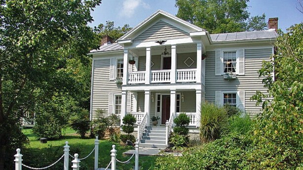 A two-story house with a front porch, a staircase leading to the entrance, and a chain-link fence in front. - Frog Hollow Bed and Breakfast (Lexington)