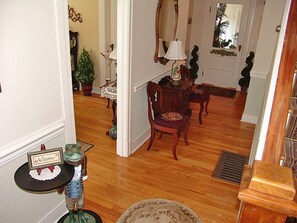 A wooden-floored hallway with a dining area featuring a table and chairs, a mirror, and a lamp.