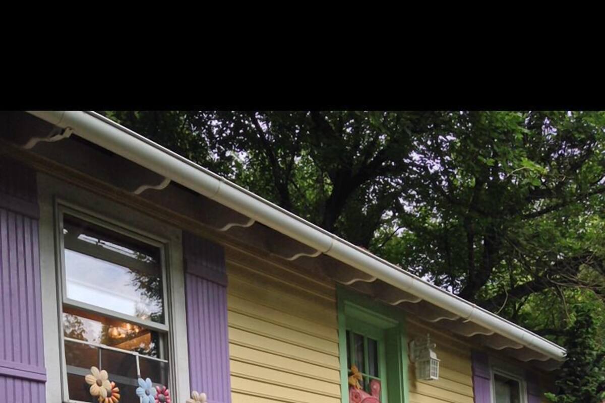 A yellow house with purple shutters, a green door, and a stone foundation.