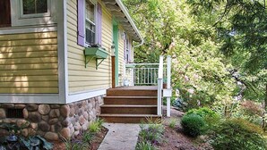 A house with a stone foundation, a front porch with steps, and a garden with various plants and a small tree. - Frog Hollow Bed and Breakfast (Lexington)
