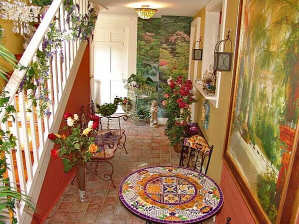A hallway with a tiled floor, a round table with a colorful mosaic, and a staircase with a white railing.