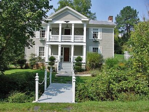 A two-story house with a front porch, a central entrance, and a small garden area. - Frog Hollow Bed and Breakfast (Lexington)