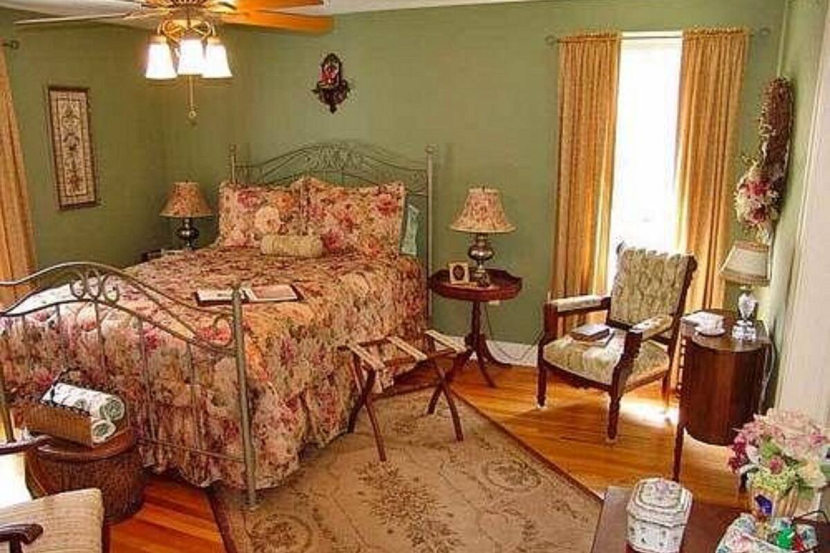 A bedroom with a four-poster bed, a wooden chair, a small round table, and a nightstand.