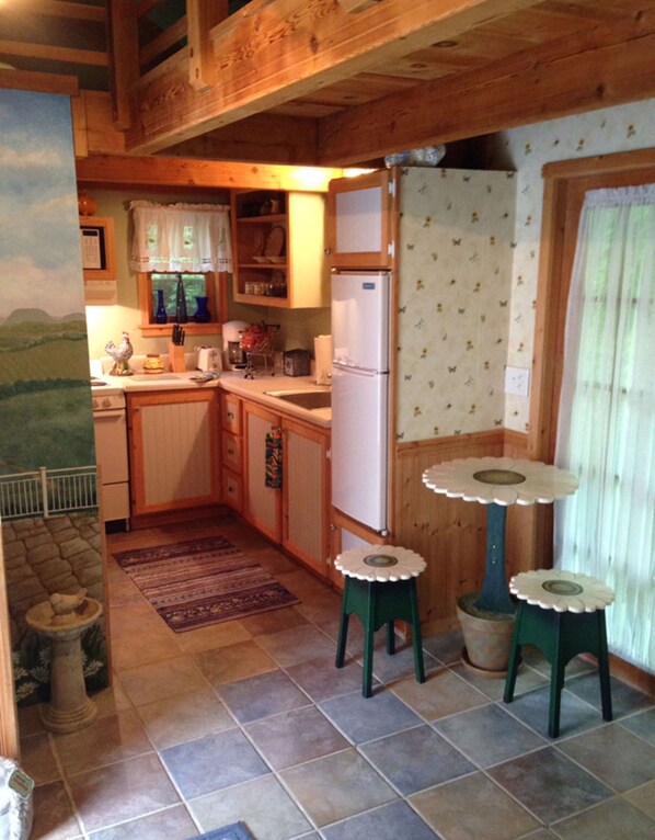 A rustic kitchen with wooden cabinets, a white refrigerator, and a small table with stools.