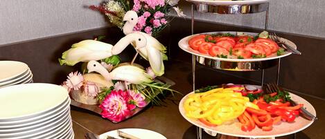 A buffet setup with various dishes, including sliced cucumbers, tomatoes, and bell peppers, arranged on a multi-tiered stand.