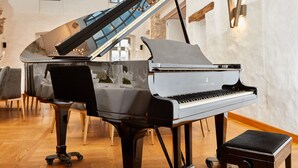 A grand piano in a spacious room with a wooden floor, a small stool, and a staircase in the background. - Hotel Rittergut Störmede (Geseke)