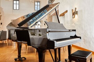 Um piano de cauda em uma sala ampla com piso de madeira, um pequeno banquinho e uma escada ao fundo.