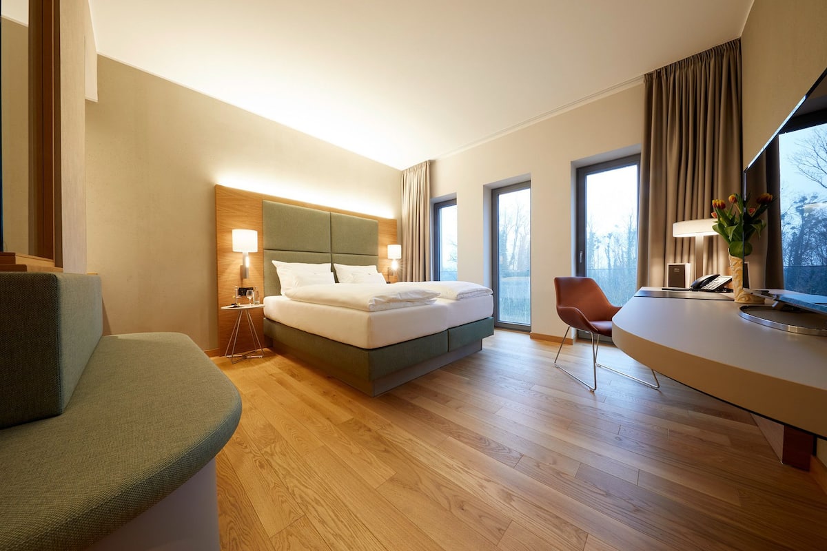 A modern hotel room with a large bed, a desk, a chair, and a sofa.