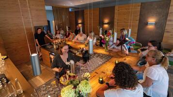 A group of people gathered around a bar area with a variety of bottles and glasses, indicating a social setting.