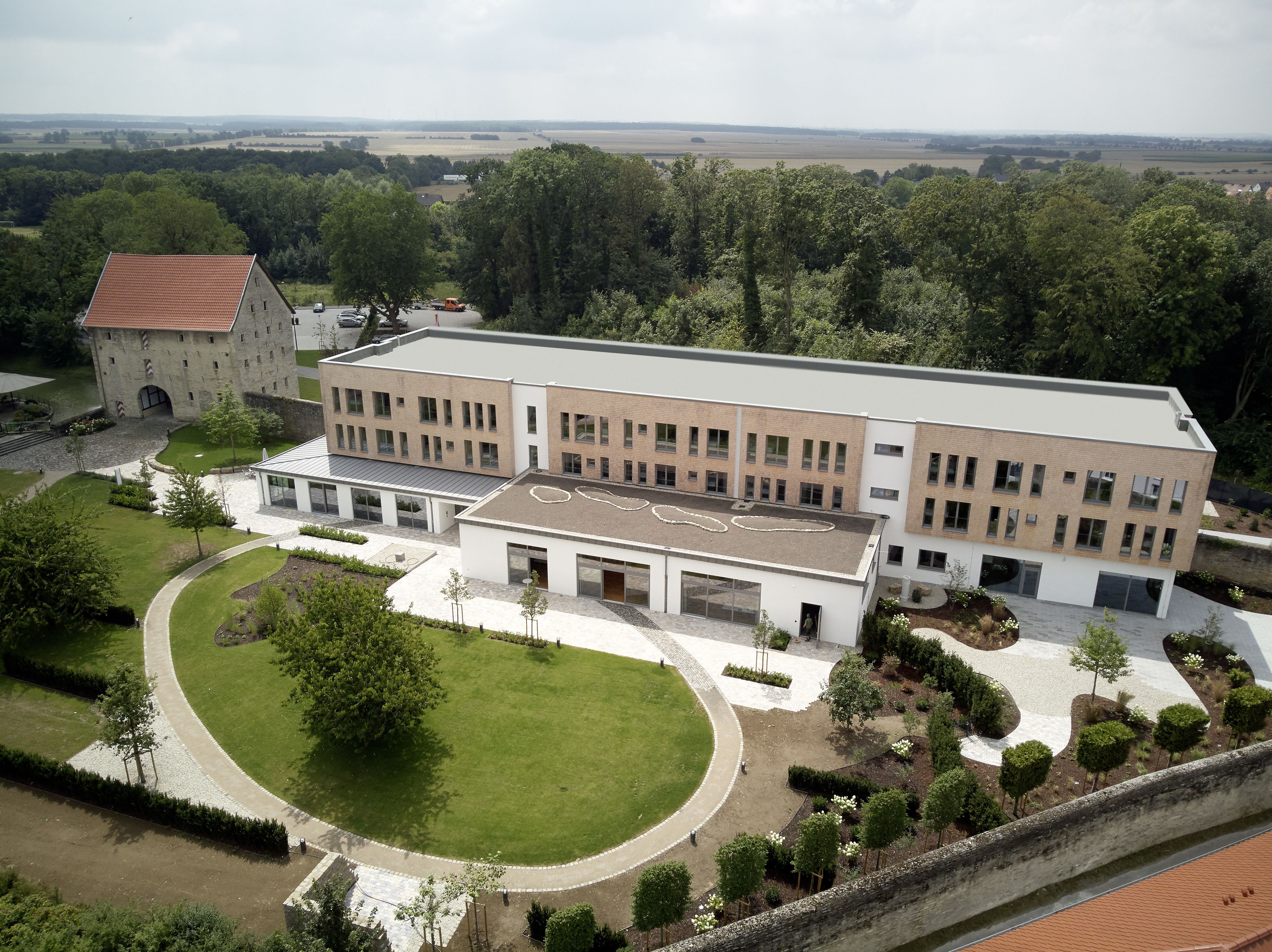 A modern building with a flat roof, surrounded by well-maintained lawns and a stone wall.