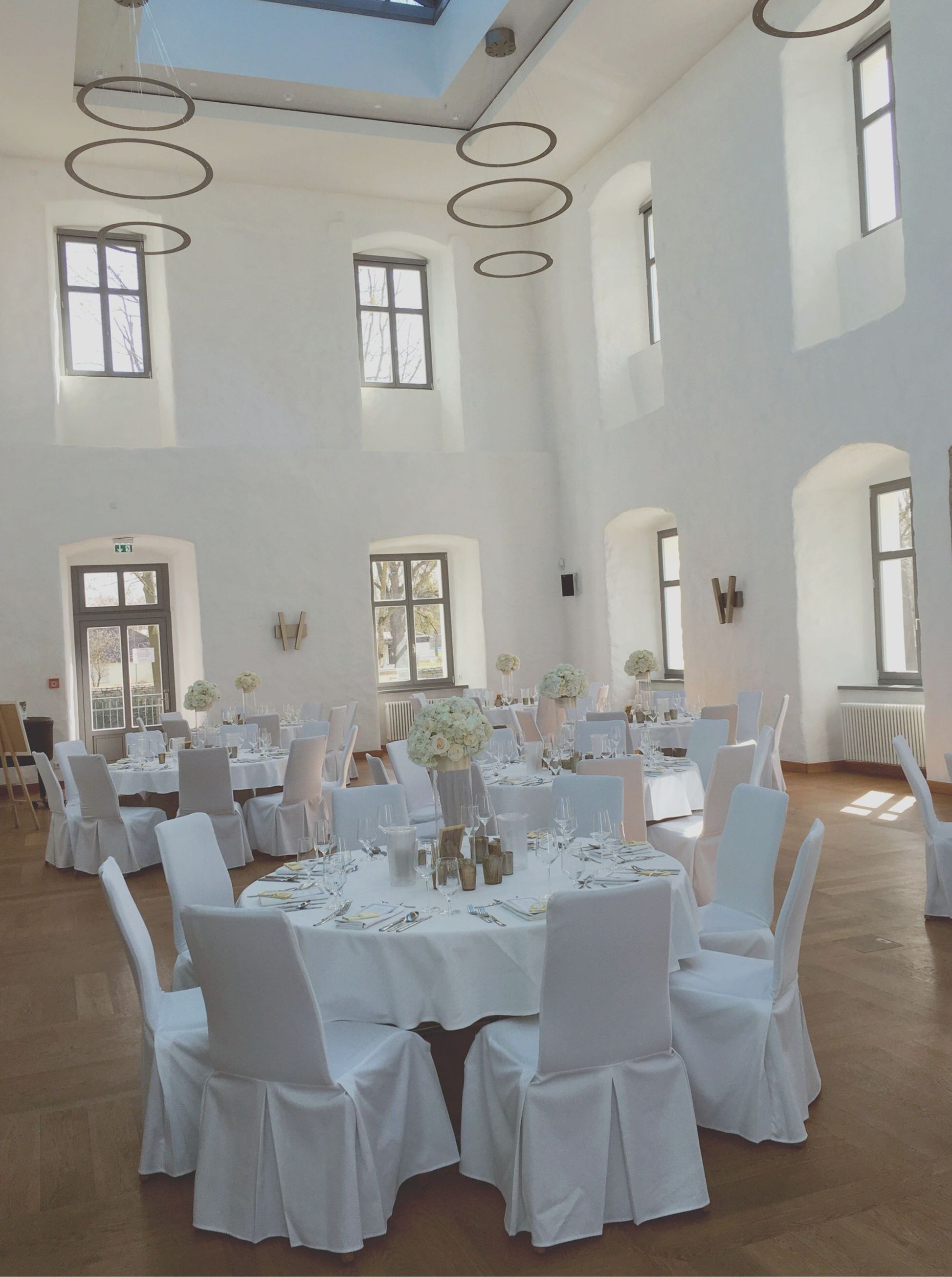 A spacious hall with high ceilings, multiple tables set for dining, and large windows allowing natural light.