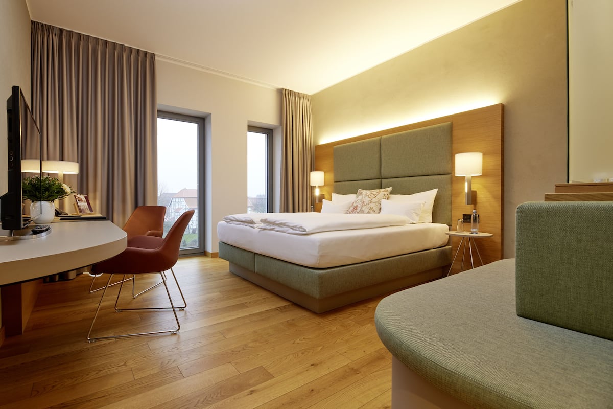 A hotel room with a bed, a desk, a chair, and a sofa.
