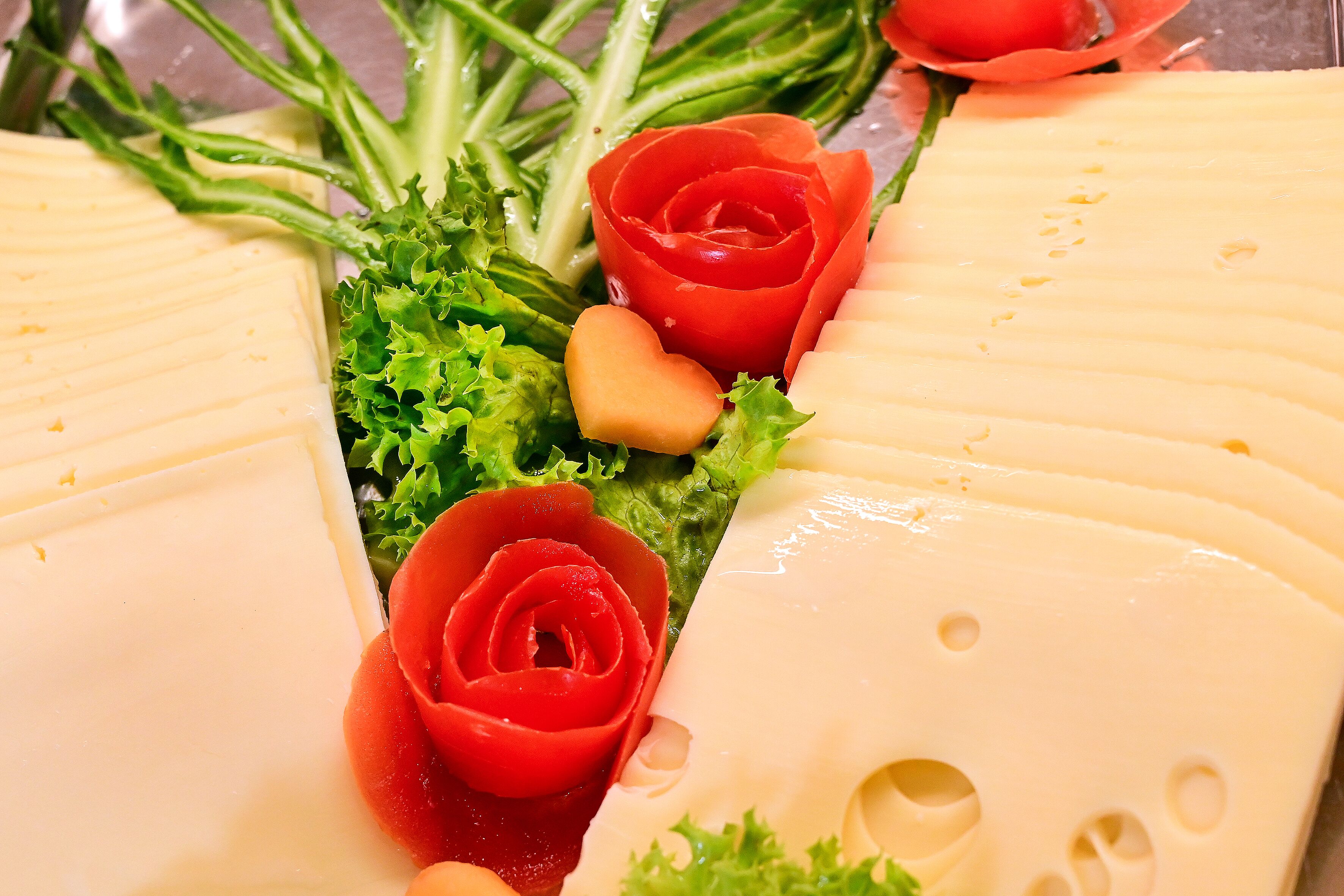 A cheese platter with various cheeses and decorative elements like a red rose and heart-shaped cheese.