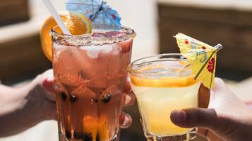 Dos bebidas, una con pajita y la otra con un adorno, sujetadas por manos.